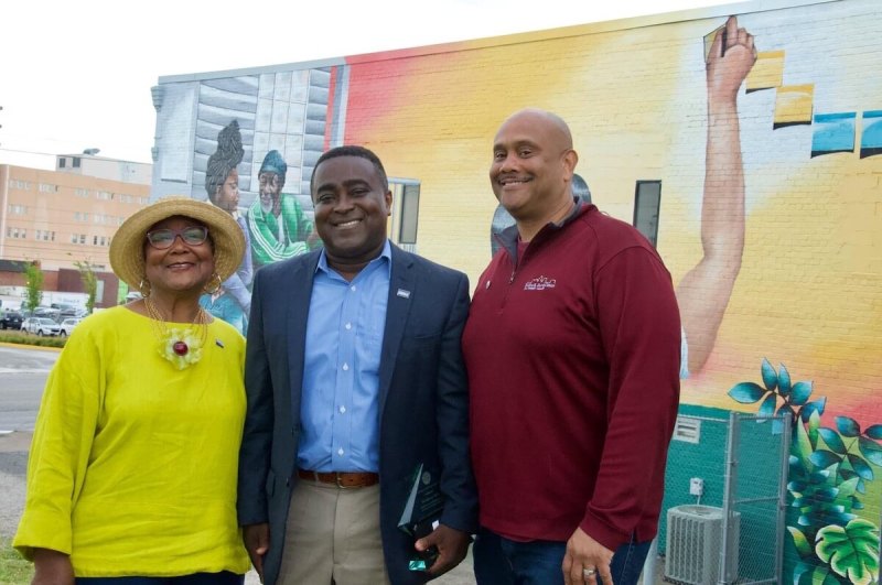 Three people smiling at the camera with a mural in the background. Ahmed Agyeman, center, is director of the Evelyn Davis Center for Working Families at DMACC as of 2021. (Photo submitted)