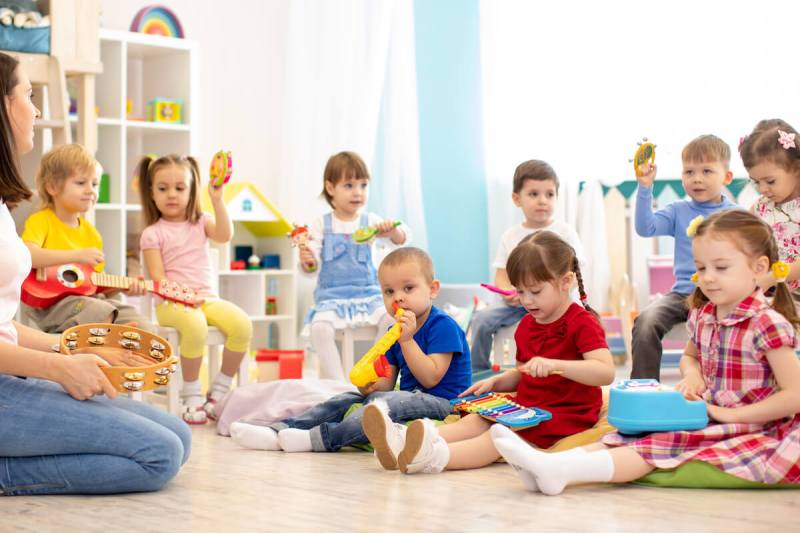 child care classroom, one teacher kneeling in front of a group of small children. Some are holding toys