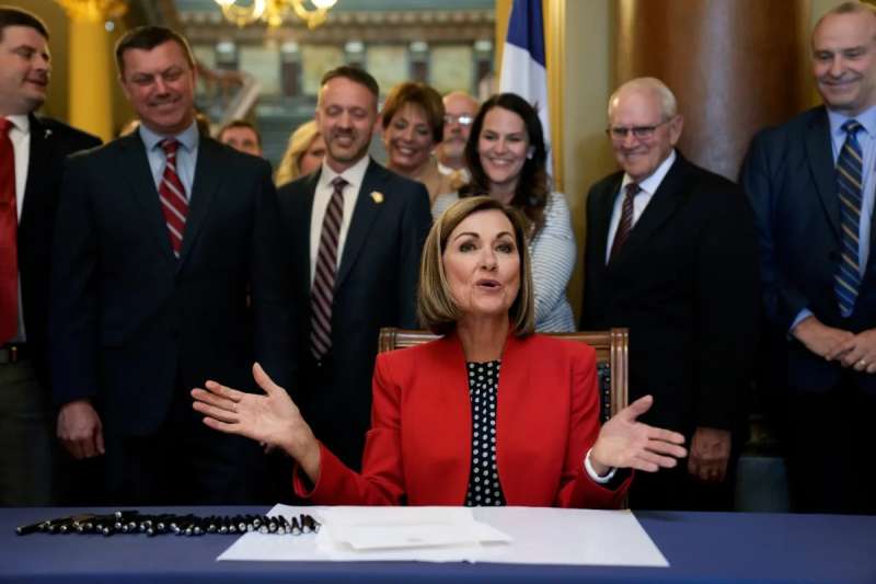 Picture of Gov. Kim Reynolds, seated, signing a bill surrounded by Iowa senators