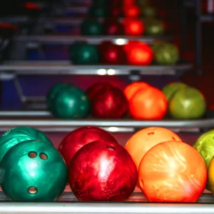 Green, red, and orange bowling balls are lined up ready to play.