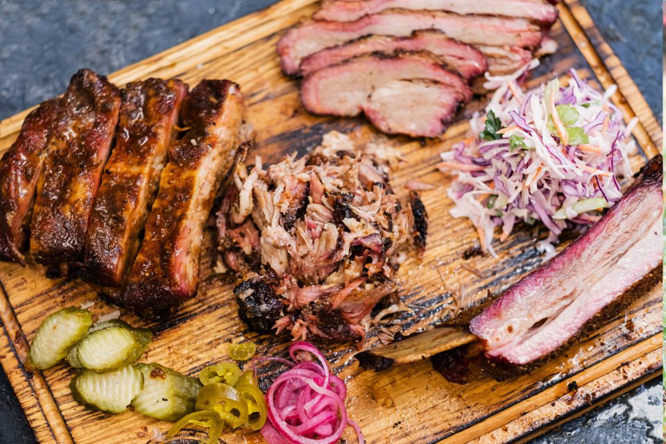 A platter of smoked meats with pickles and pickled red onions.