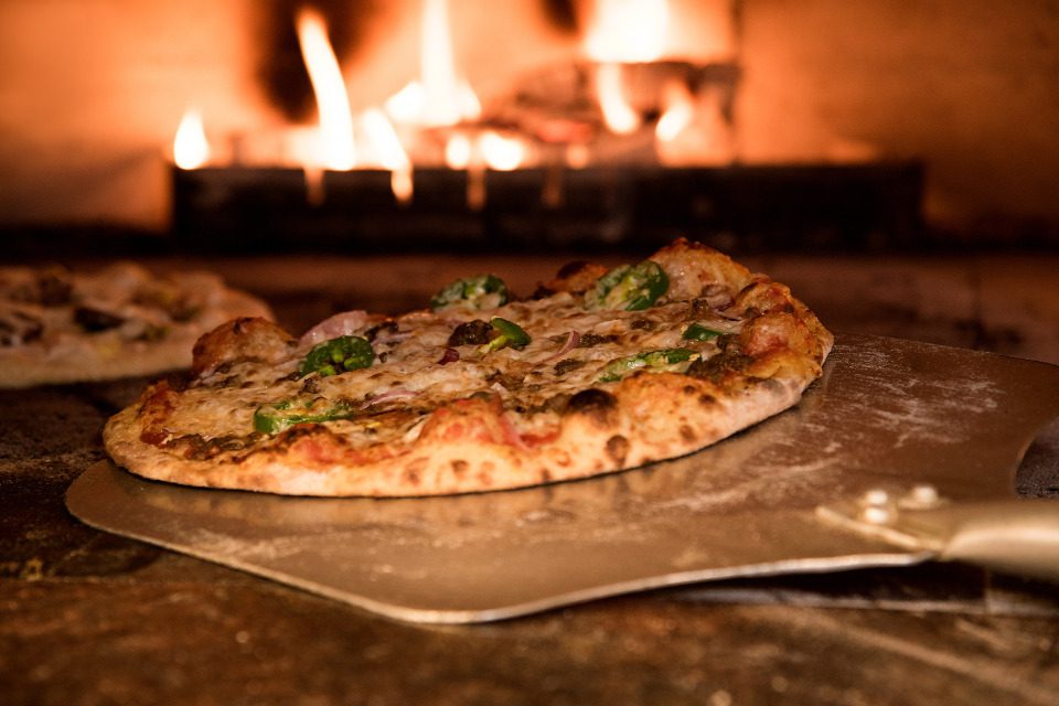 A pizza coming out of a wood fired oven.