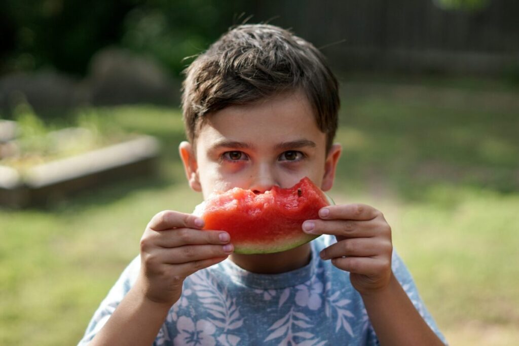 Young boy holding up a piece of half-eaten watermelon.