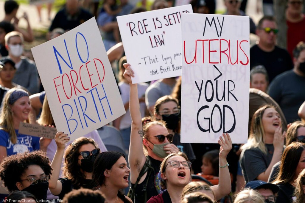 FILE, abortion-rights protesters from a 2022 rally in Des Moines. Three signs are visible. One says "No forced birth." Another says: "'Roe is settled law' - That lying piece of shit Brett Kavanaugh" The last one says "My uterus > your God."