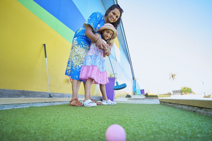 Mother helping child to play mini-golf