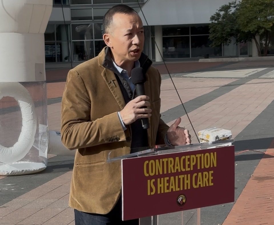 Democratic challenger Lanon Baccam speaks to a crowd in front of a sign reading "Contraception is health care."