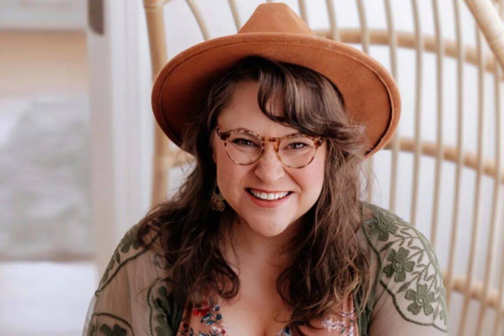 headshot of Sarah Ashby, a smiling white woman with glasses and a hat.