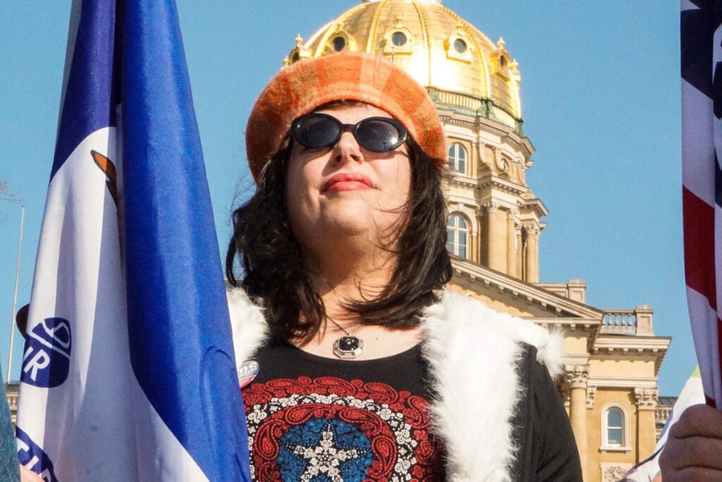 Aime Wichtendahl standing in front of the Iowa Capitol, holding the Iowa State Flag.