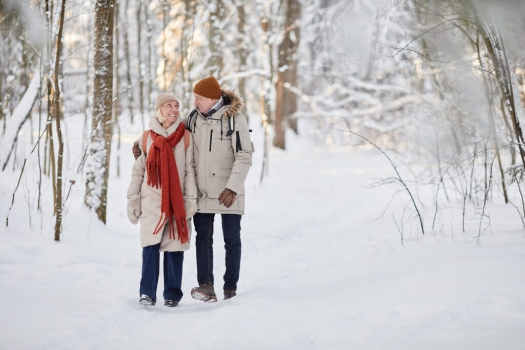 Full length portrait of happy senior couple enjoying walk in winter forest and looking at each other, copy space.