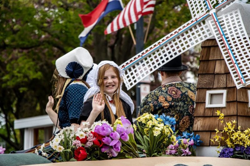 A young girl in costume waves from a float in a parade during Tulip Time Festival.