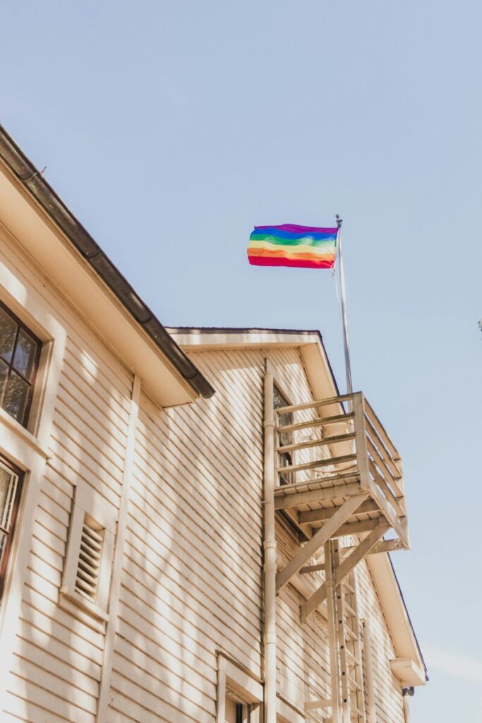 A pride flag flies above a wooden house. (Diogo Fagundes/Unsplash)