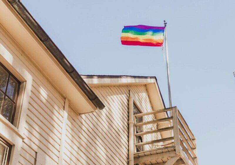 A pride flag flies above a wooden house. (Diogo Fagundes/Unsplash)