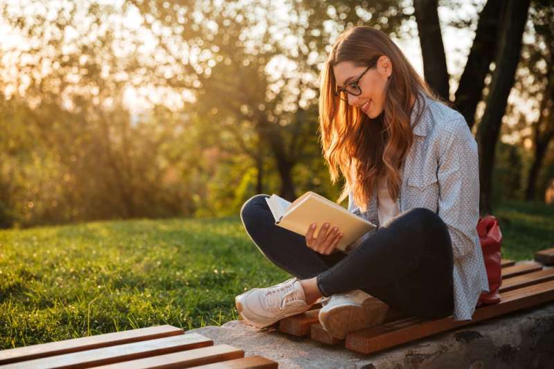 a woman sits outside and smiles while reading an iowa author
