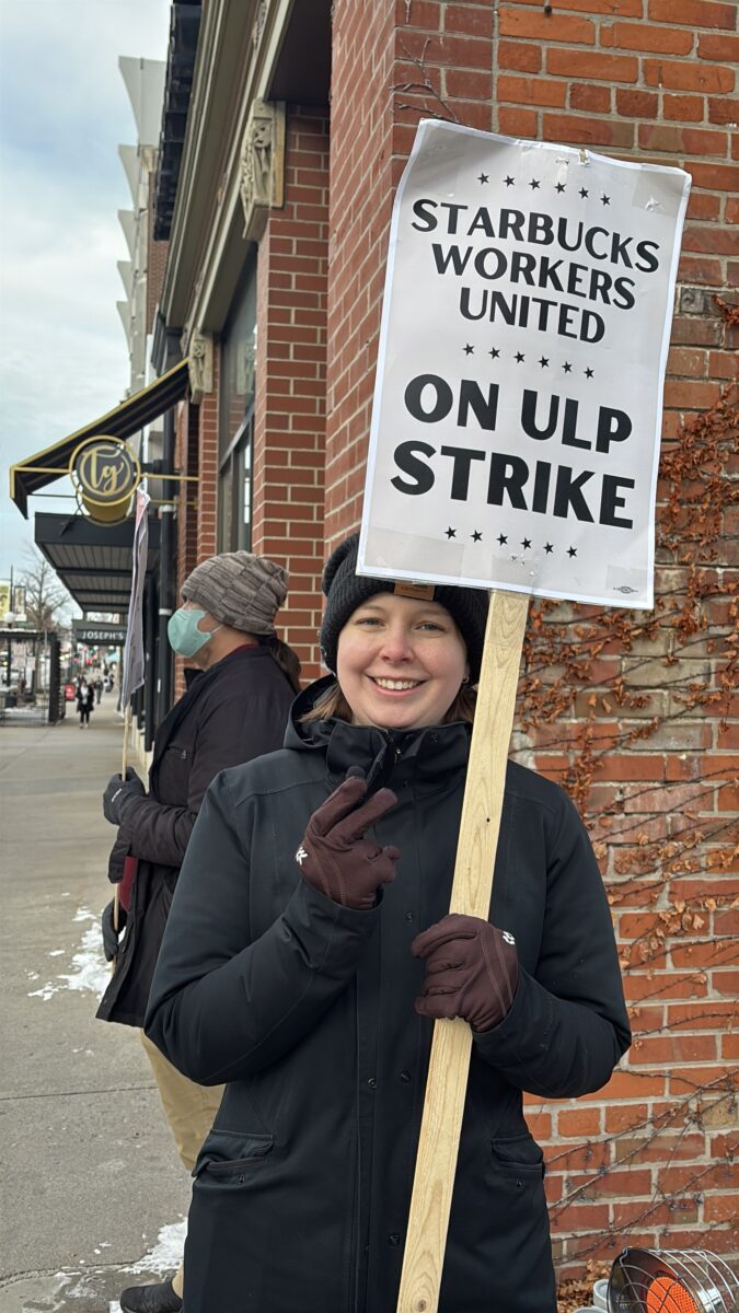 Abigail Scheppmann, a barista at the Starbucks in Iowa City and an organizing committee member for her store's Starbucks Workers United union, poses for a photo while picketing outside the store Dec. 19, 2025. (Amie Rivers/Iowa Starting Line)