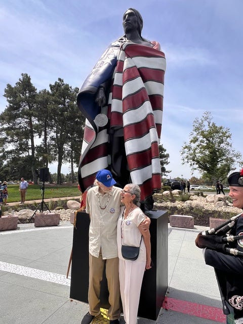Tom Schomberg and his wife stand in front of the statue