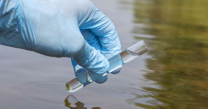 Someone scoops up water from an outdoor source into a test tube
